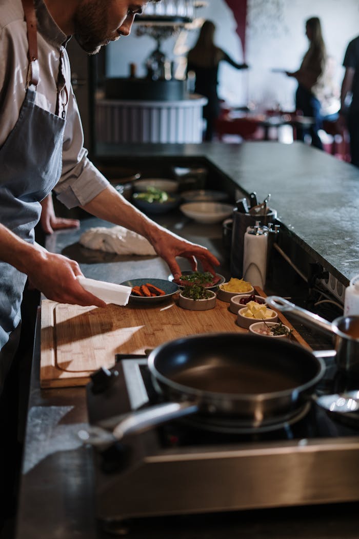 Chef in an apron plating small dishes at a professional kitchen pass